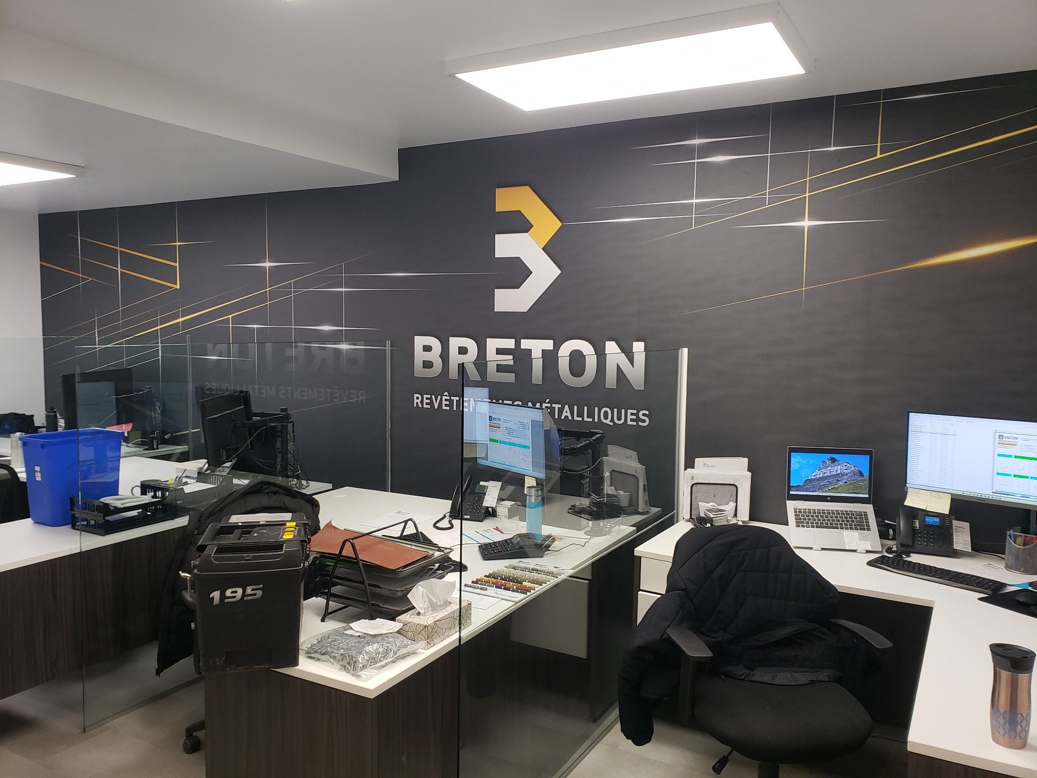 Murale Breton sur fond sombre avec logo et lignes graphiques jaunes derrière plusieurs postes de travail.