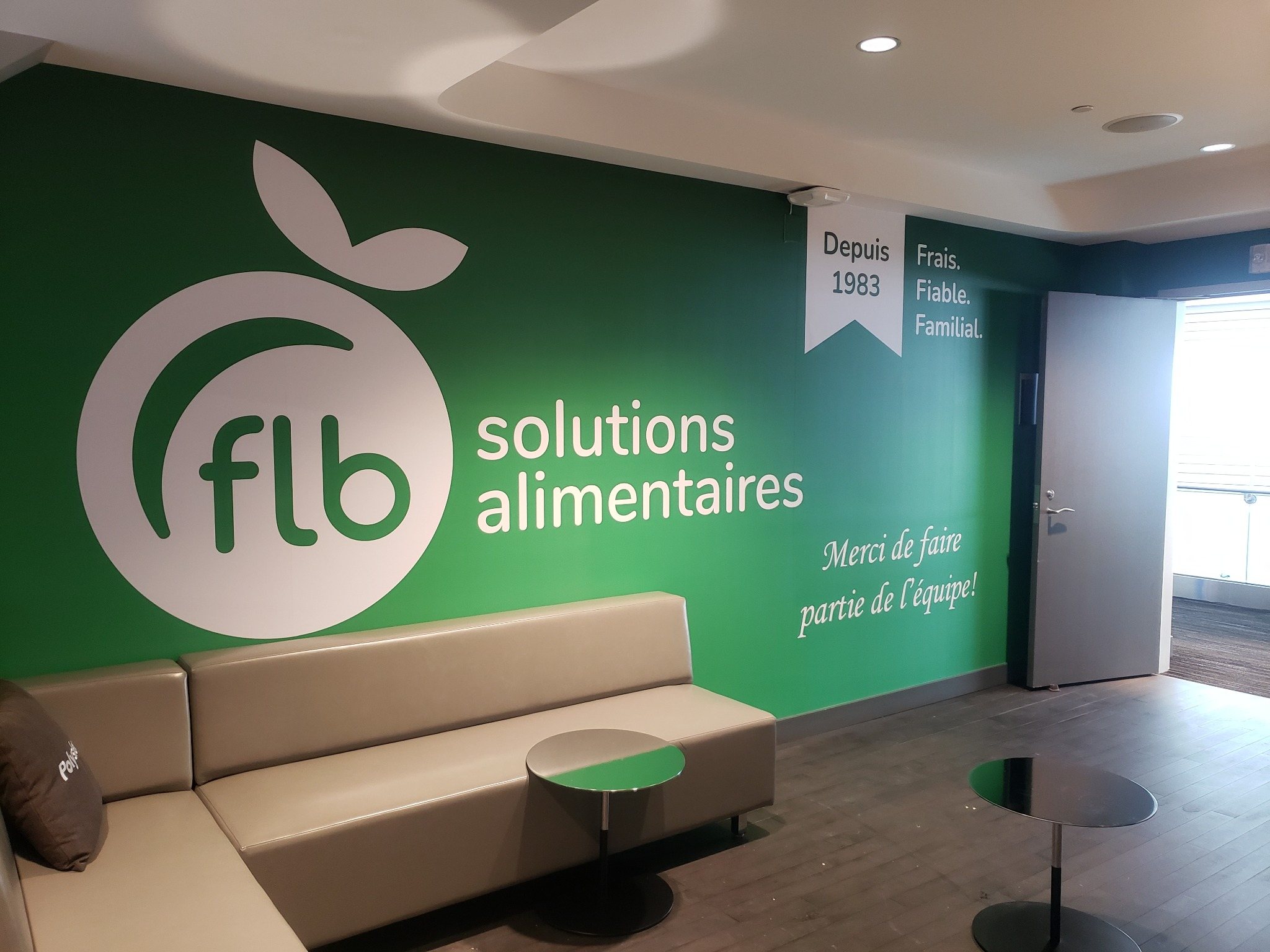 Mur vert avec le logo blanc de FLB Solutions alimentaires derrière une banquette et des petites tables.