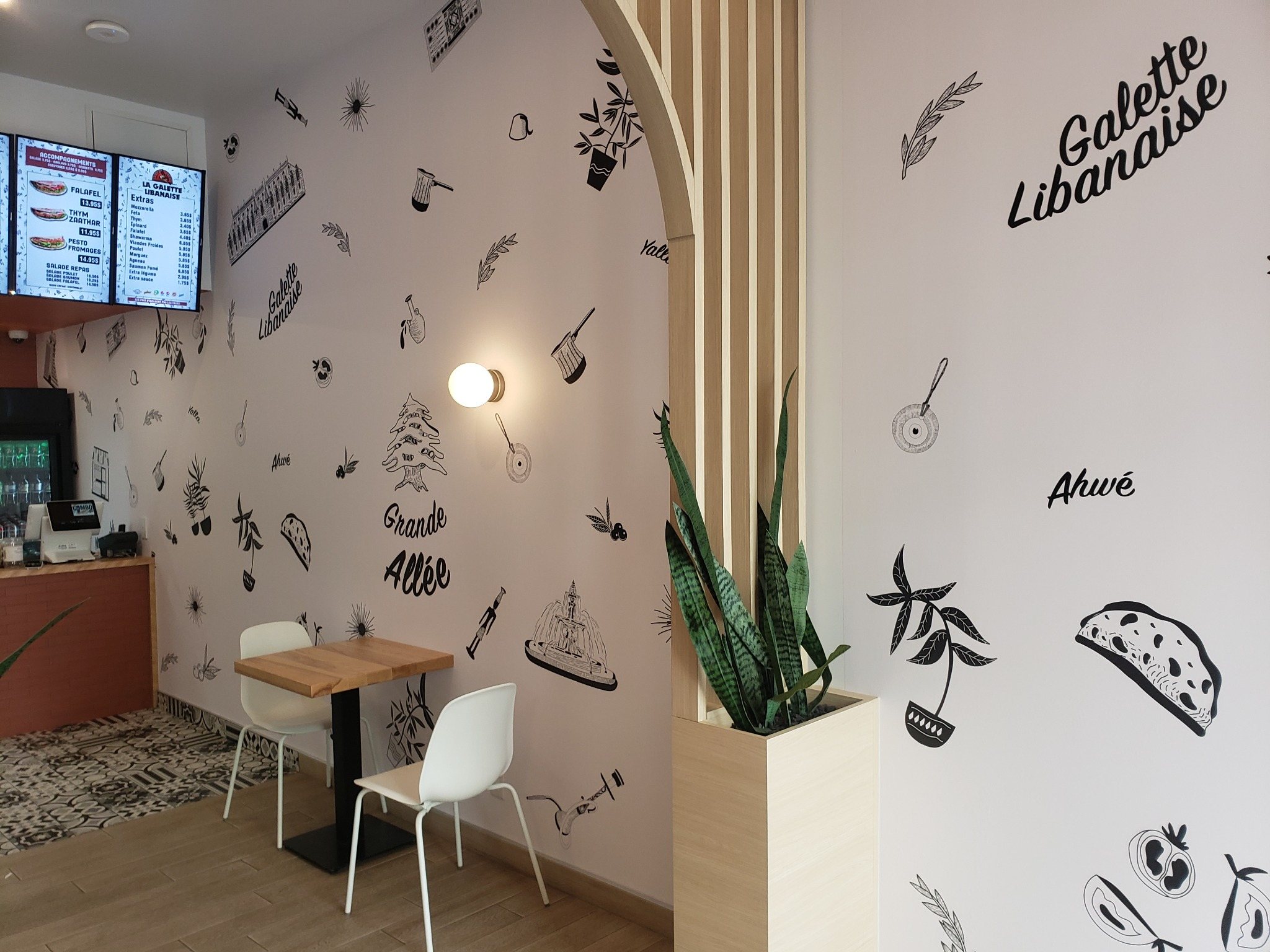 Murs du restaurant Galette Libanaise décorés d’illustrations culinaires noires, avec le nom du restaurant au-dessus d’une table.