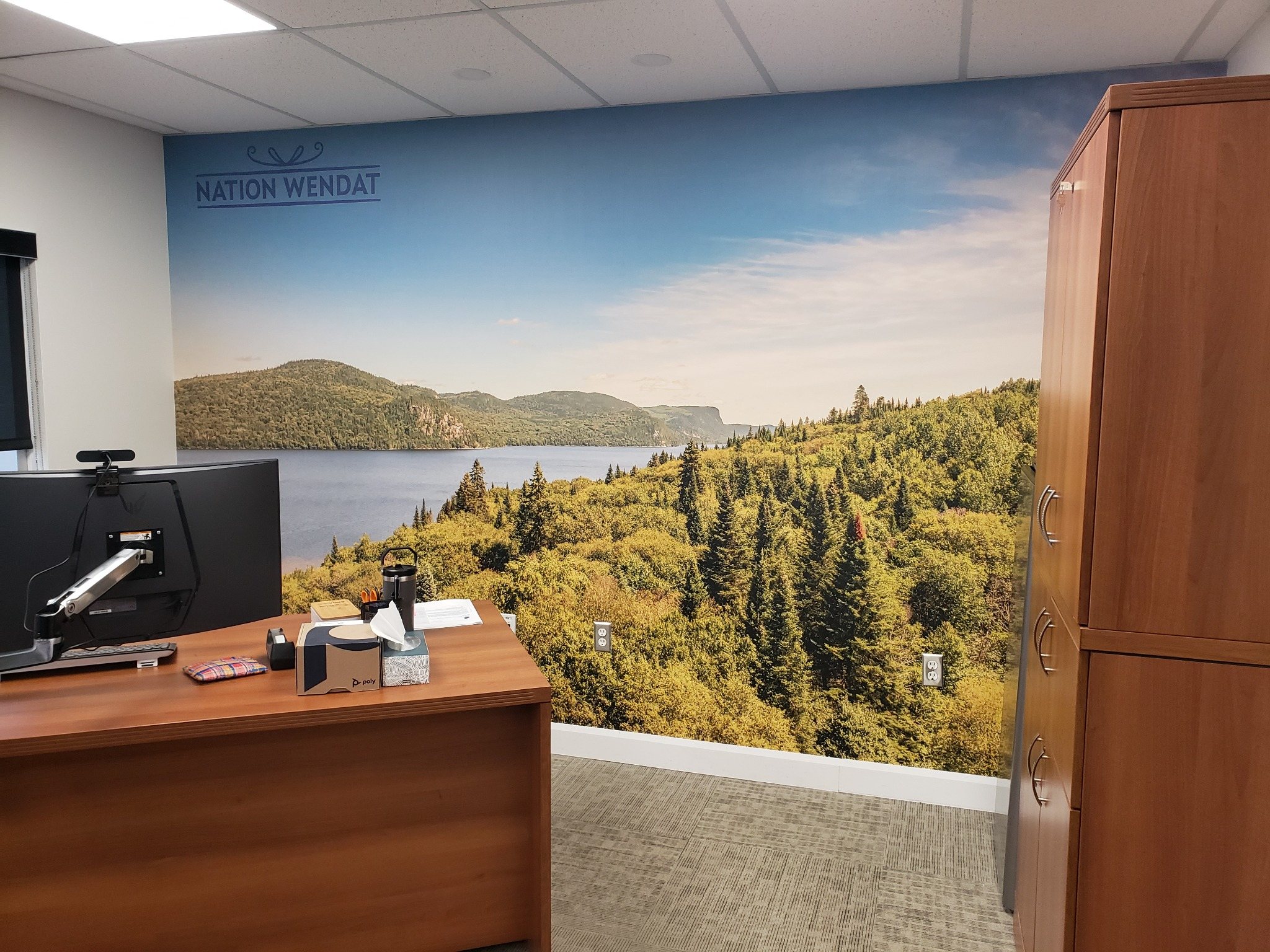 Murale panoramique de lac, forêt et relief avec l’inscription Nation Wendat, installée derrière un bureau.