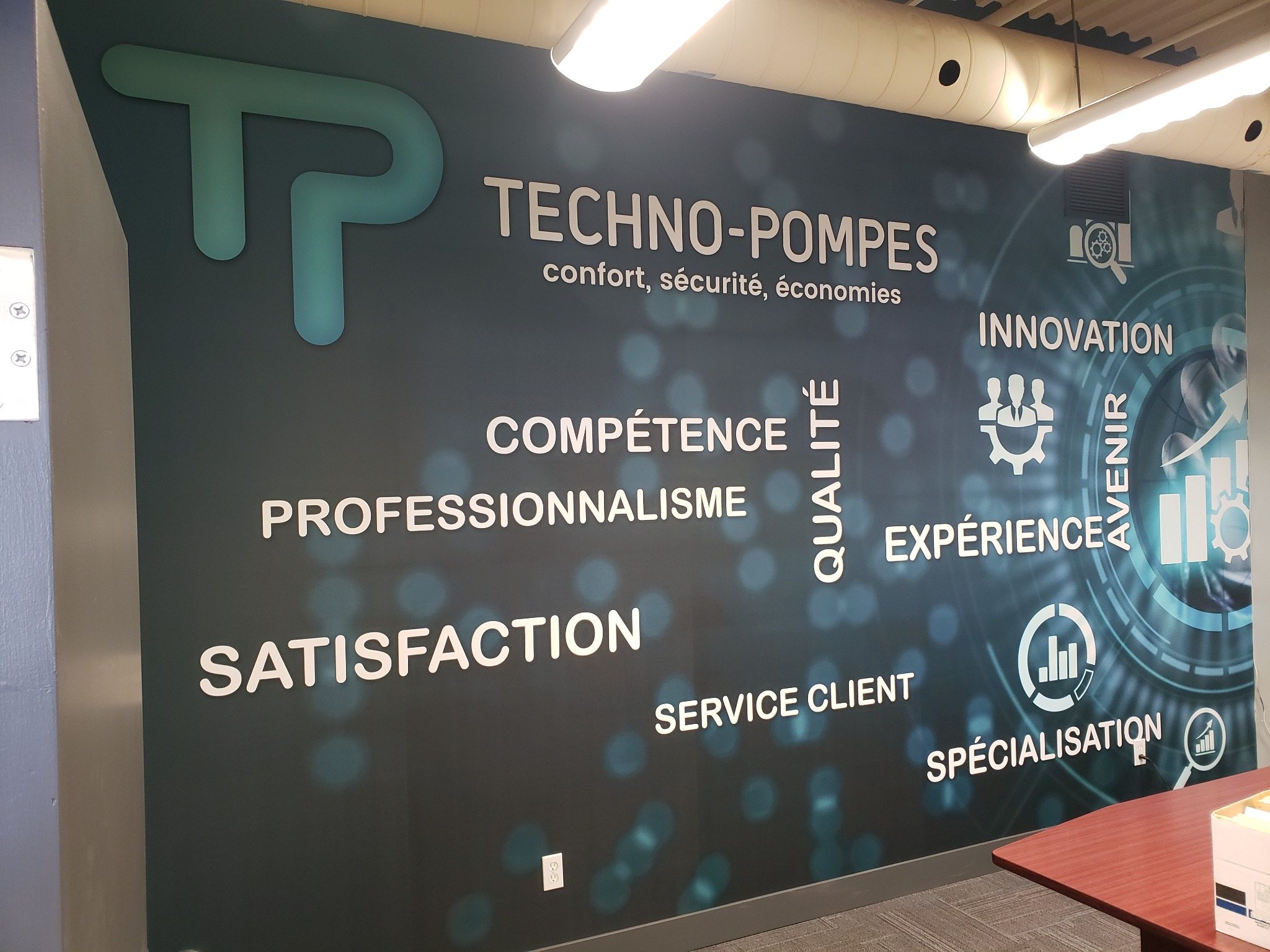 Murale Techno-Pompes avec logo, mots-clés et visuel technique sur un mur d’entreprise.